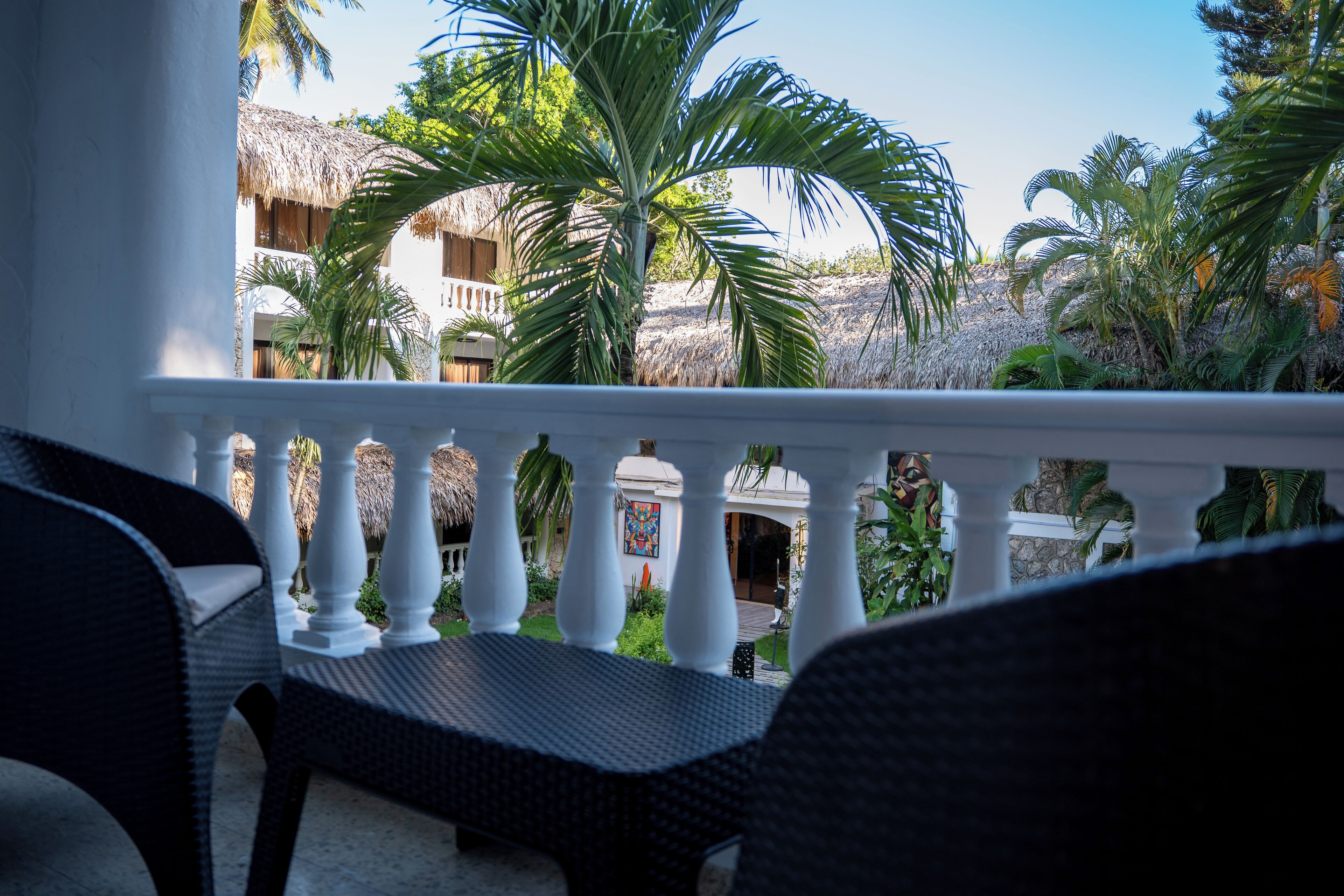 Un balcone con mobili in vimini, ringhiere bianche e piante tropicali.