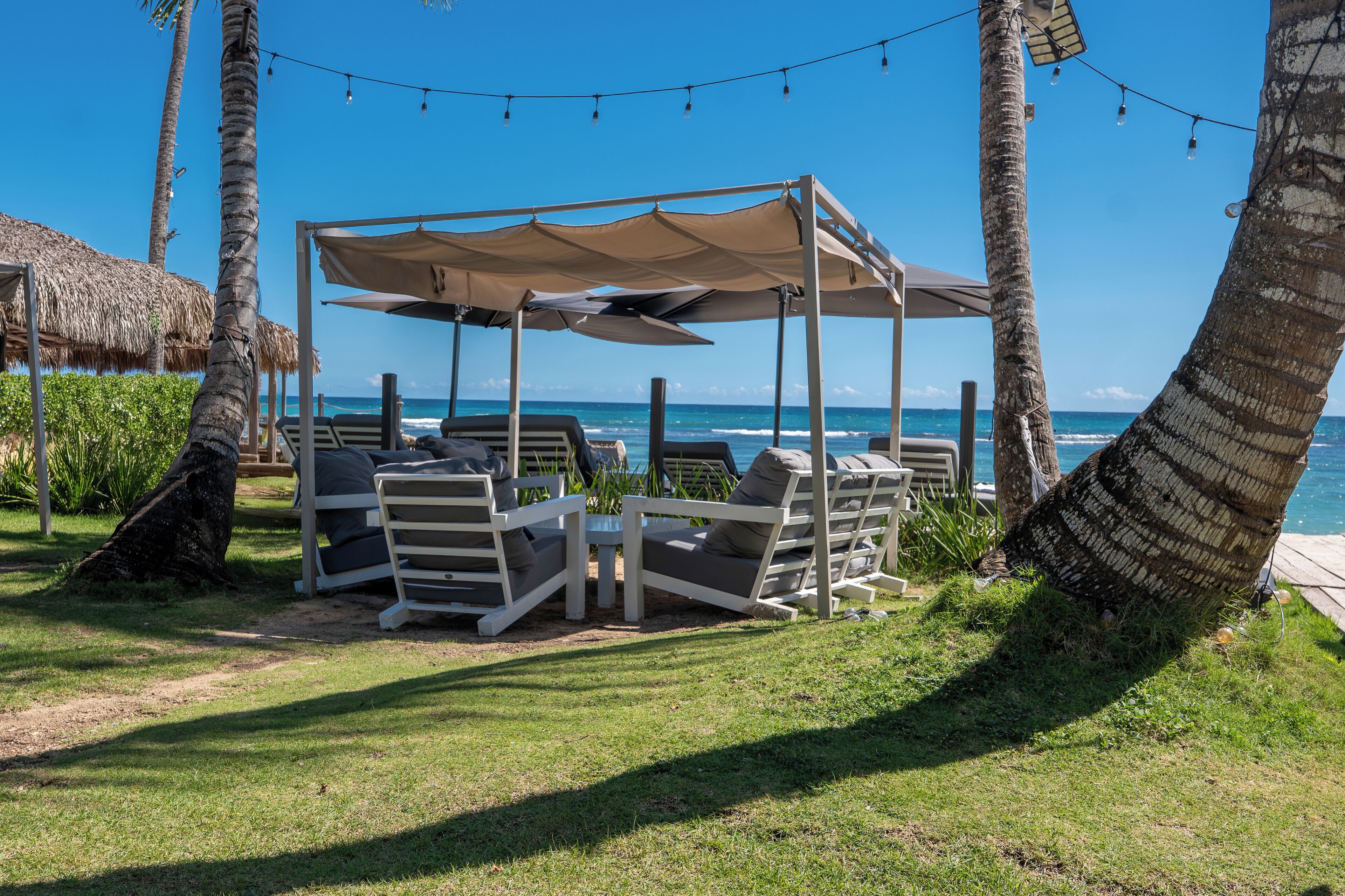 Un área de descanso junto a la playa con toldo, sillones y vista al océano.