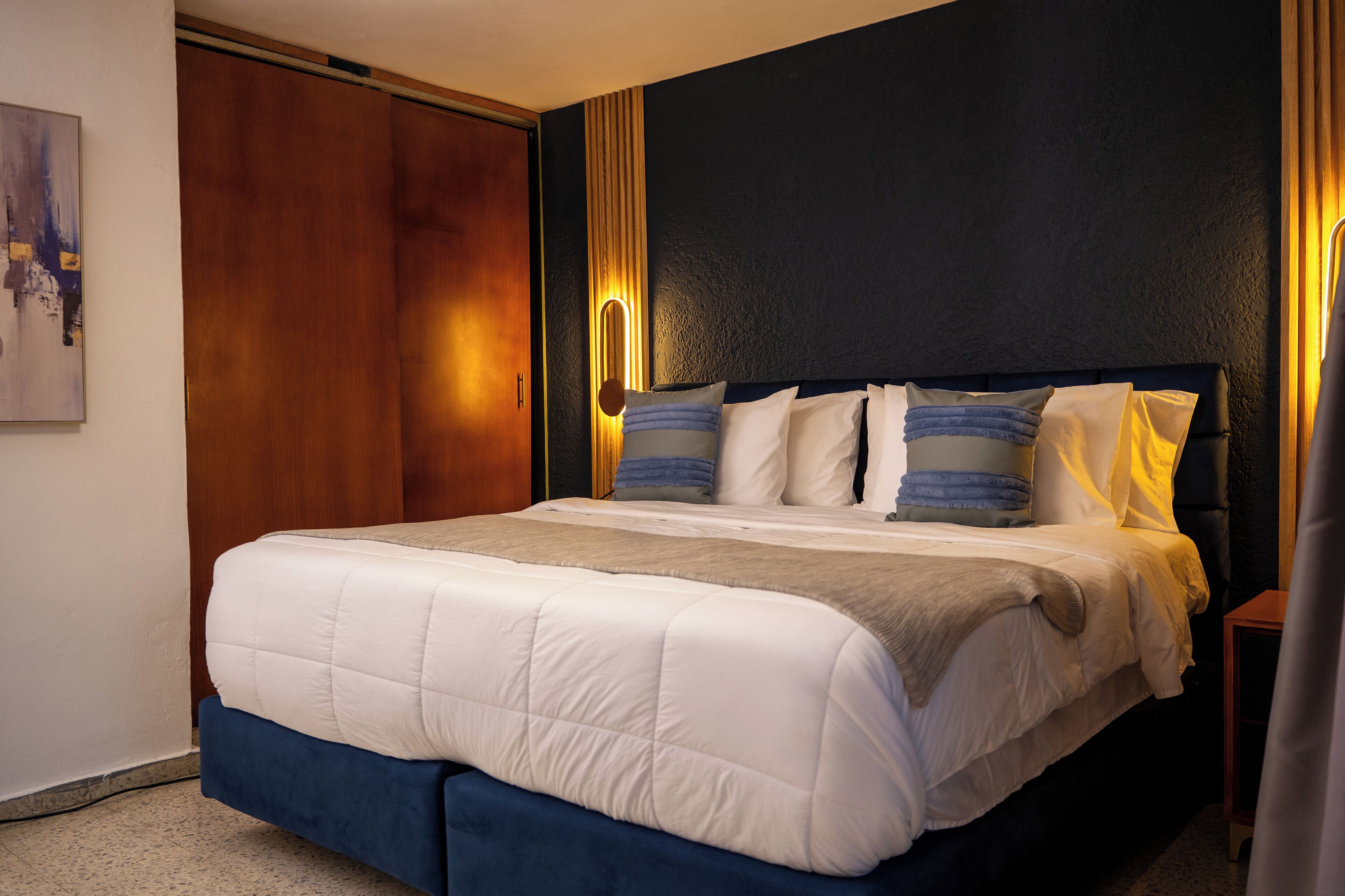 Un lit bien fait, agrémenté d’une touche de bleu, une armoire en bois et un luminaire fixé au mur.