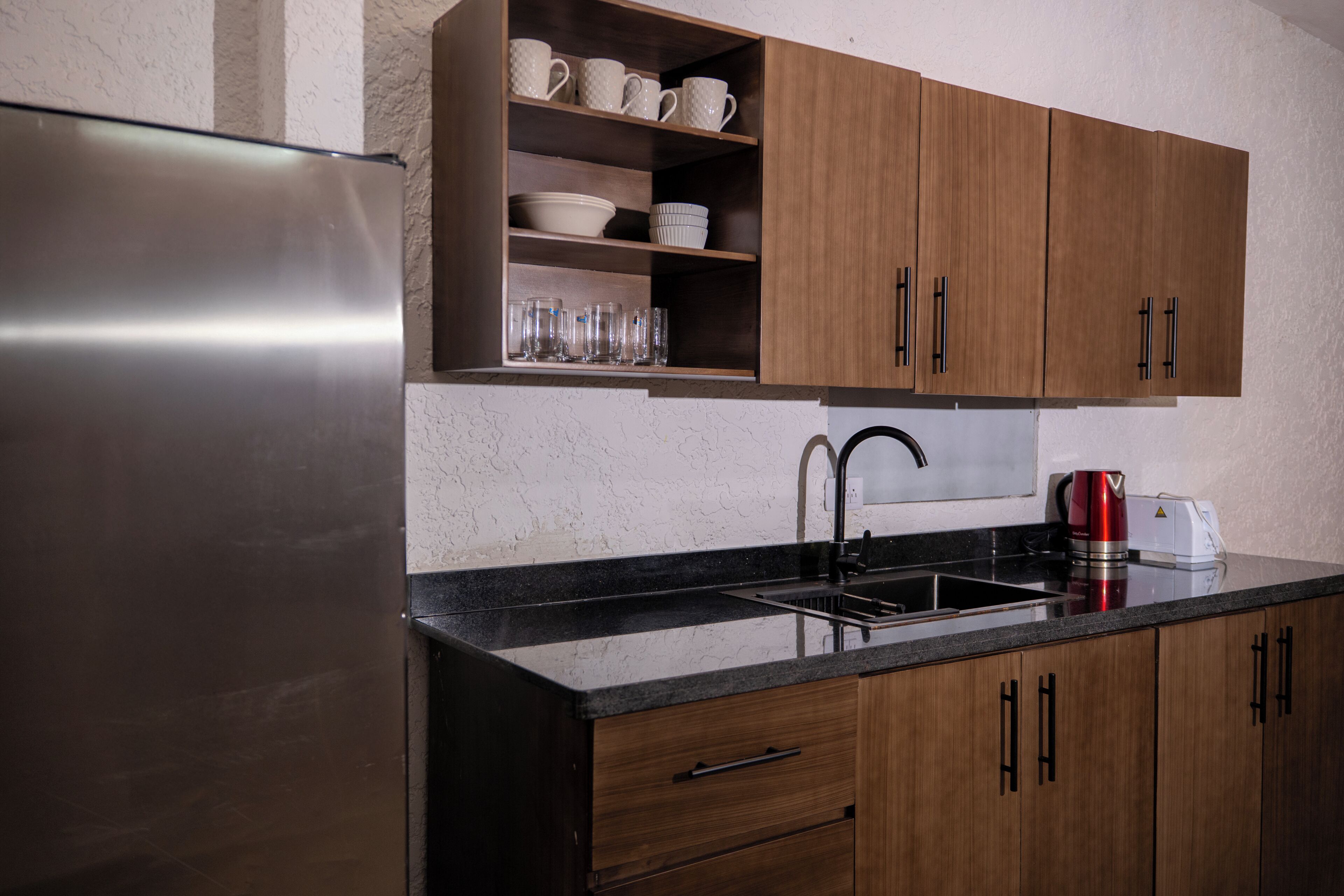 Una cocina con un refrigerador de acero inoxidable, armarios de madera, una encimera negra y una cafetera.