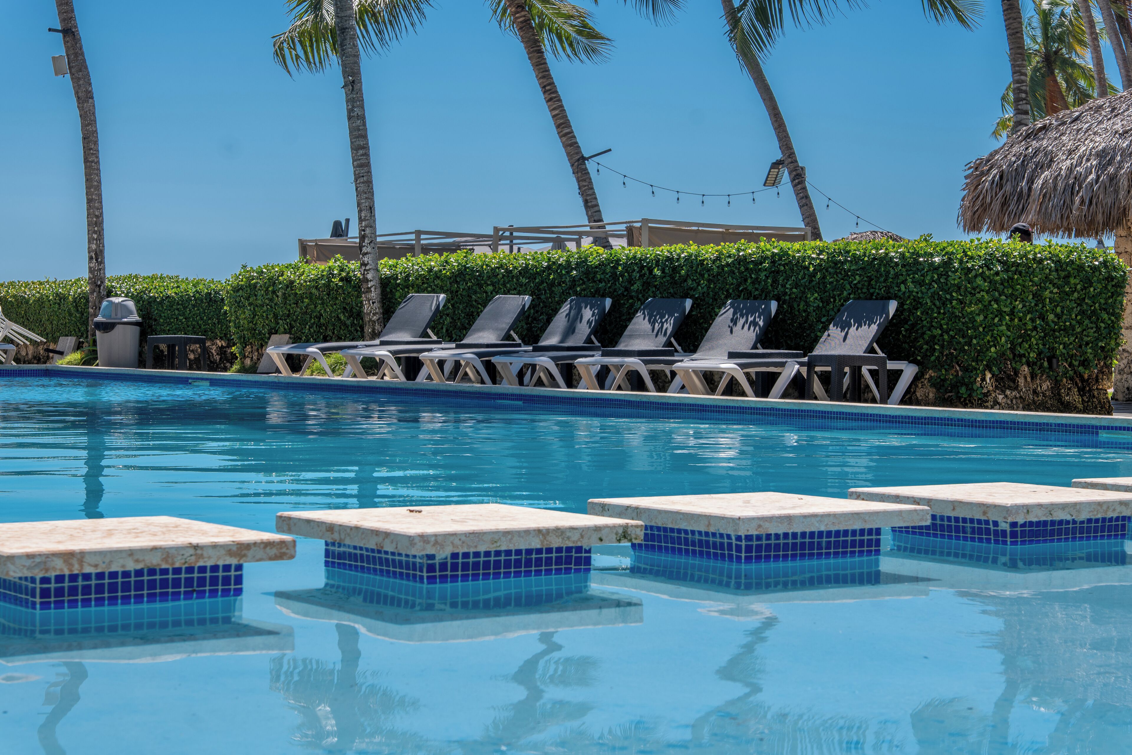 A swimming pool with lounge chairs and a thatched-roof structure.