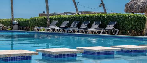 A swimming pool with lounge chairs and a thatched-roof structure.