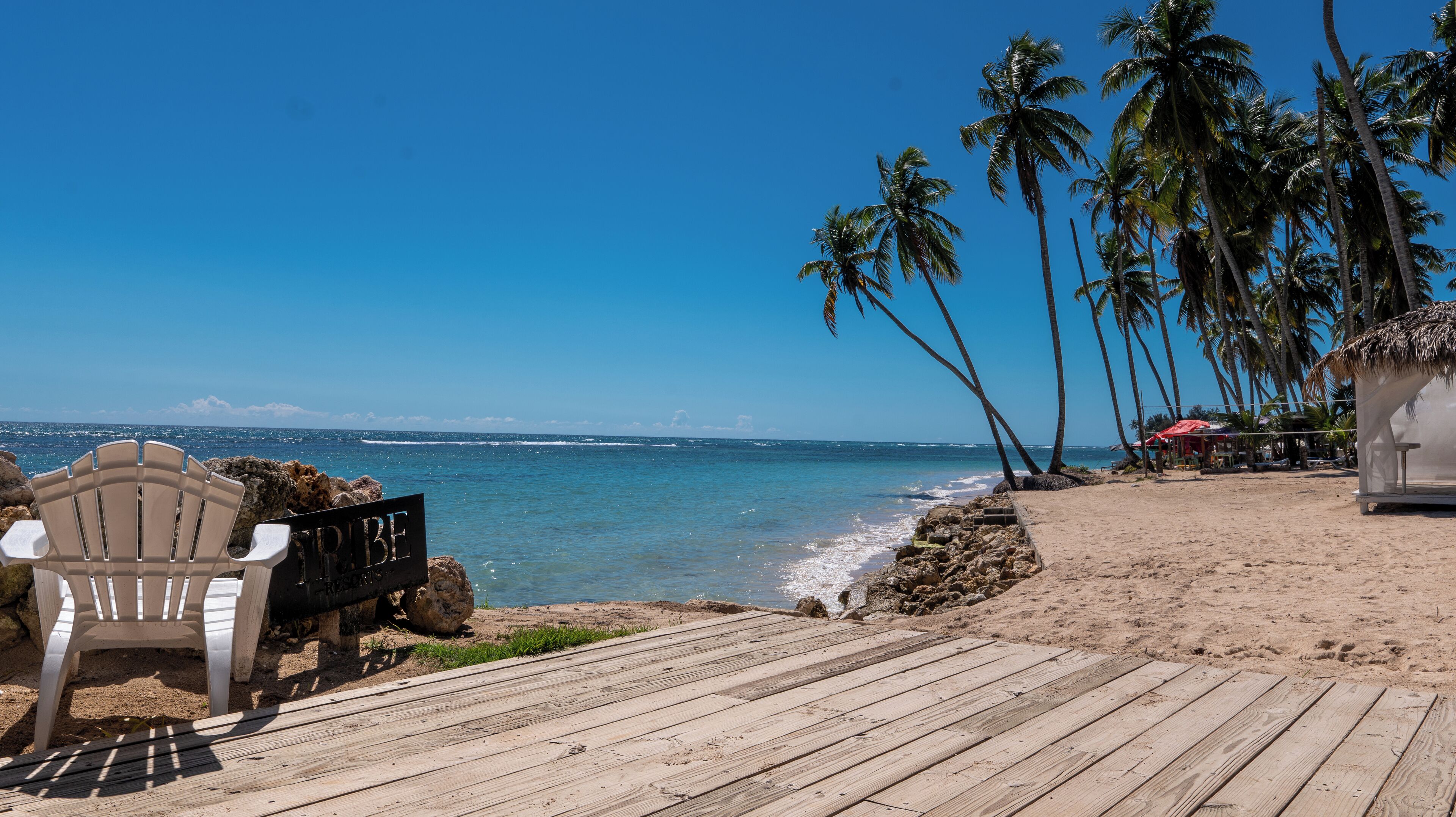 A beach with a wooden deck, a chair, and a sign that reads "TRIBE".