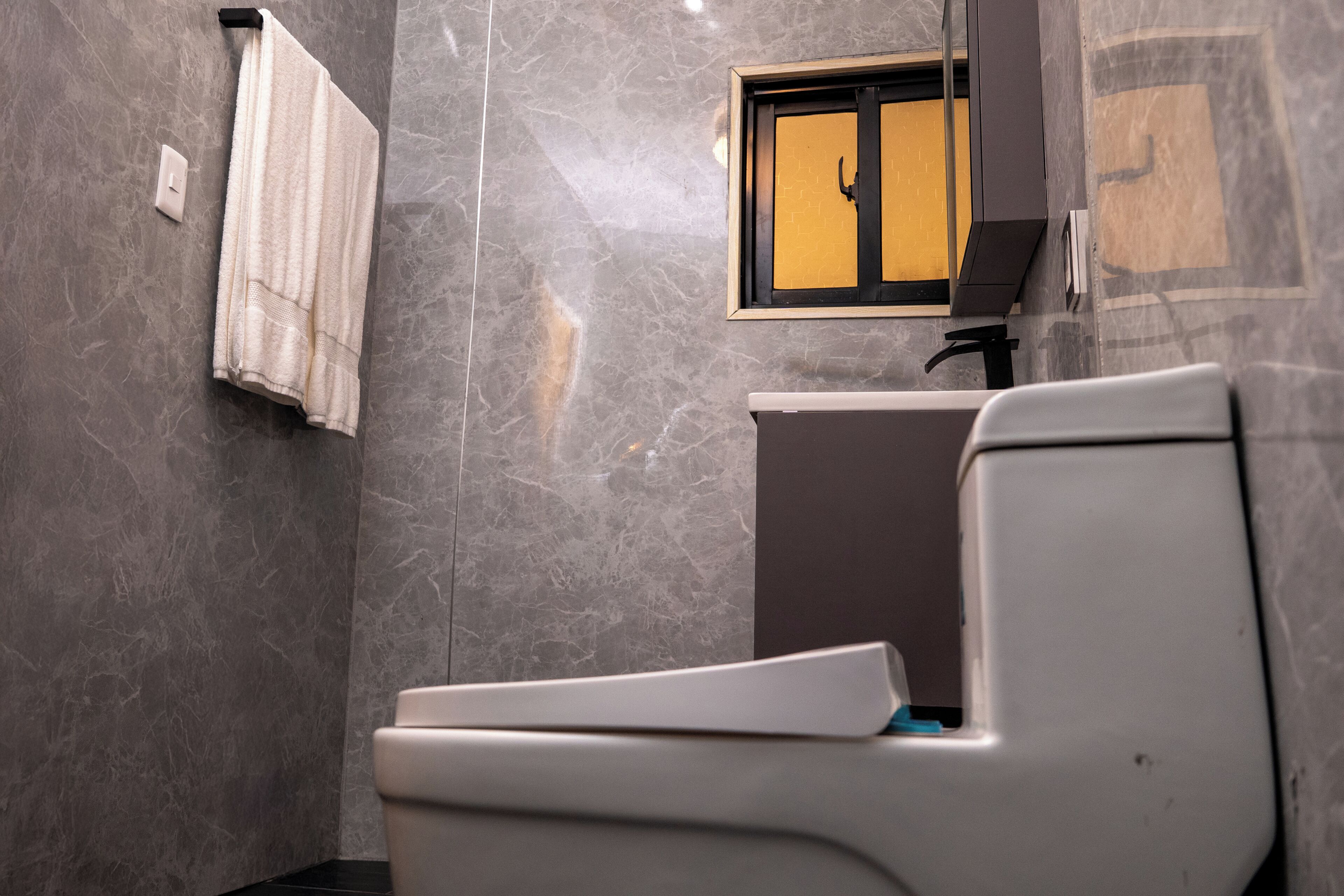 A bathroom with a toilet, a towel rack, and a window with a view of a building.