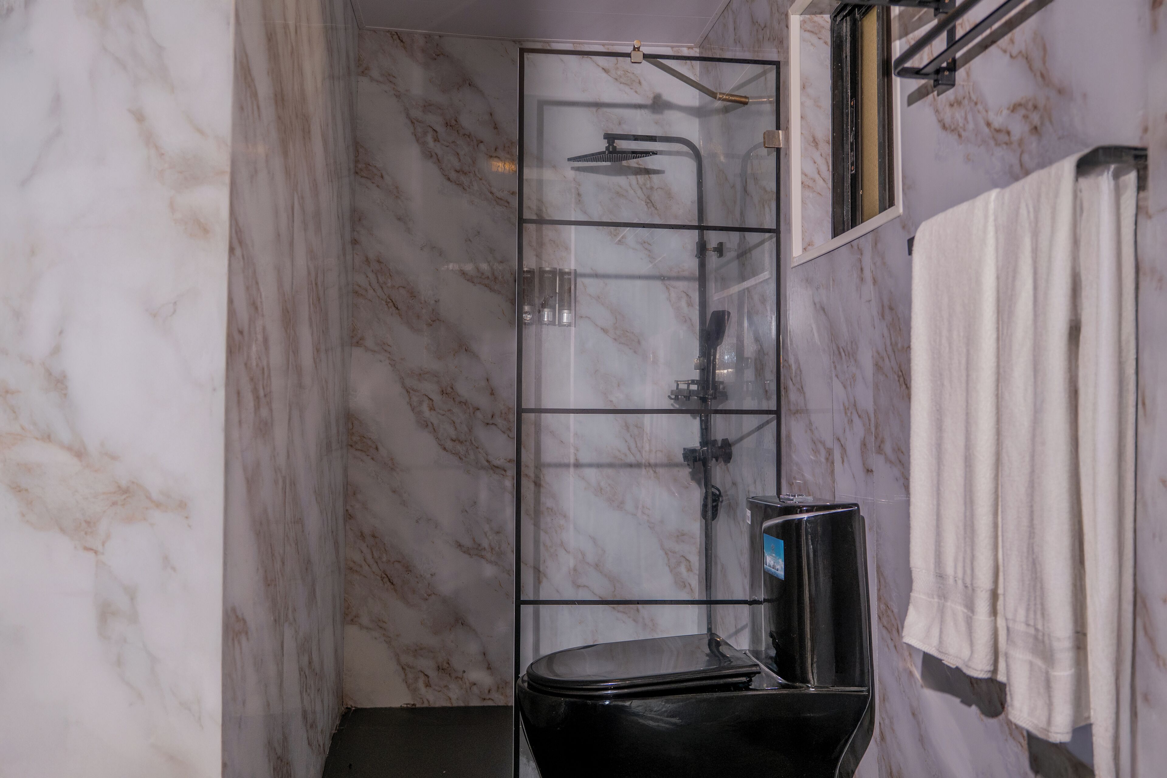 A modern bathroom with a glass shower enclosure, marble walls, and a black toilet.