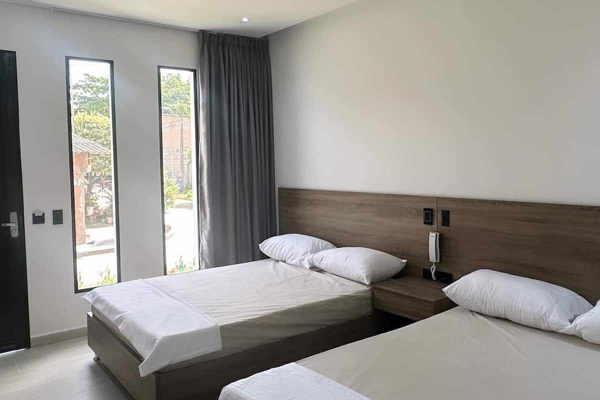 Une chambre d’hôtel moderne avec deux lits, une tête de lit en bois, un téléphone sur la table de chevet et une grande fenêtre avec des rideaux.