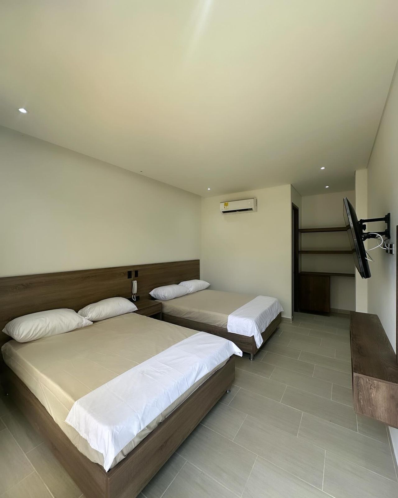 A hotel room with two beds, a TV mounted on the wall, and an air conditioning unit.