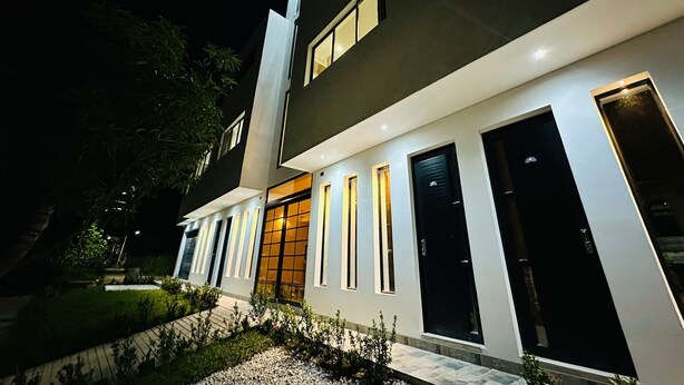 A modern two-story house with a well-lit exterior, large windows, and a visible door. - Hotel La Casona San Sebastian  (Puerto Triunfo)