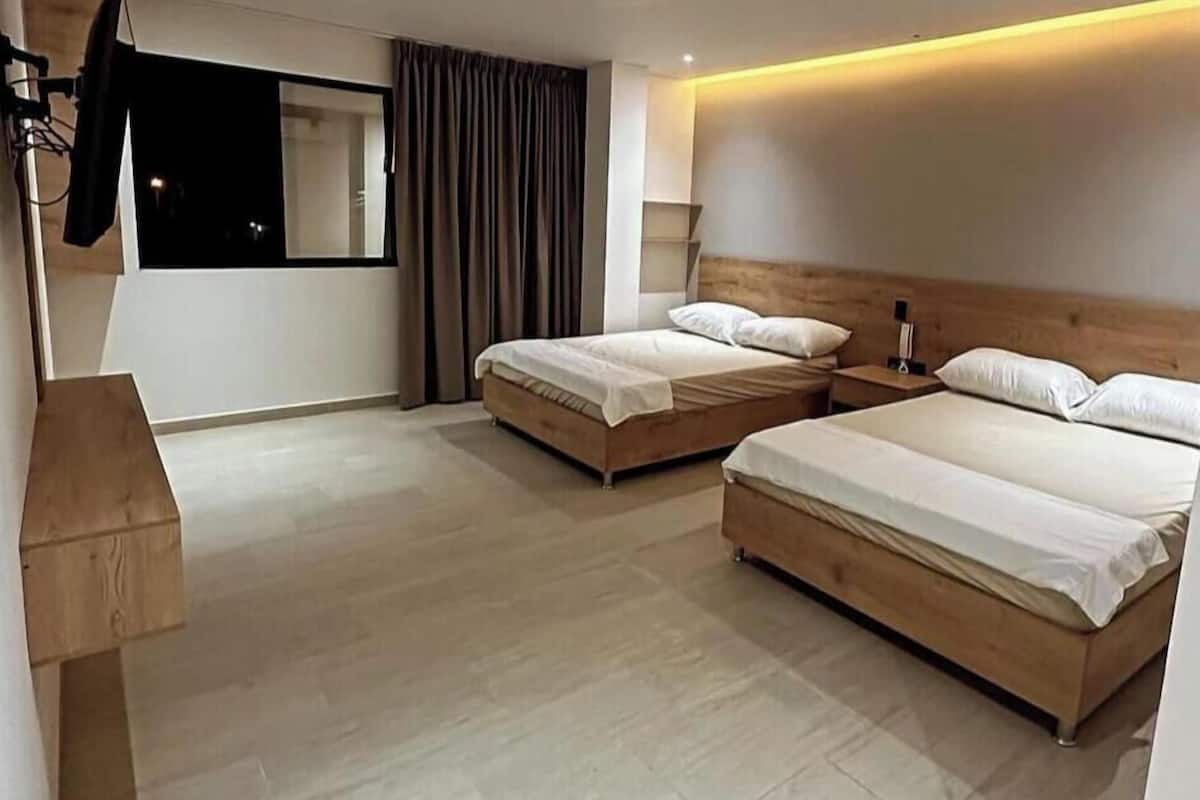 Une chambre d’hôtel avec deux lits, une tête de lit en bois, une grande fenêtre avec des rideaux et un banc en bois.
