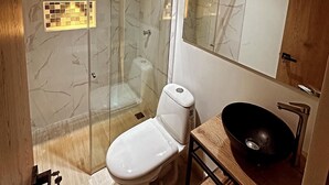 A modern bathroom with a glass-enclosed shower, a white toilet, a wooden vanity with a black sink, and a mirror above the sink. - Hotel La Casona San Sebastian  (Puerto Triunfo)