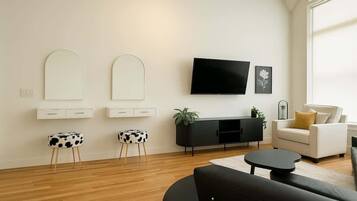 A modern living room with a black sofa, a white armchair, a black coffee table, and a flat-screen TV mounted on the wall. There are two white cabinets with mirrors and a black entertainment unit with a plant.