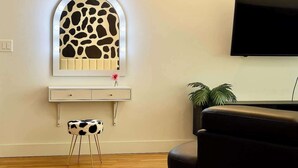 Une pièce comprenant une coiffeuse avec un miroir, un petit tabouret, une télévision et une plante.