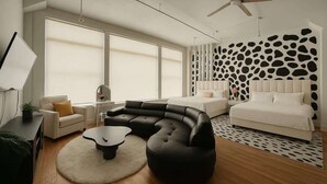 Une chambre moderne avec un canapé noir aux lignes courbes, un lit blanc et un ventilateur de plafond.