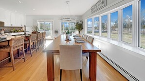 A spacious kitchen with wooden cabinets, a large dining table, and a view of the outdoors through large windows. - Scenic 4BR/3BA Waterfront Getaway with private dock, kayaks & Stunning Views (Dartmouth)