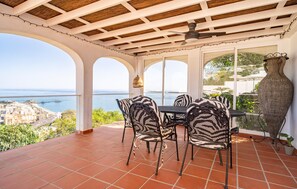 Une terrasse avec une table et des chaises, un ventilateur de plafond et une vue sur la mer.