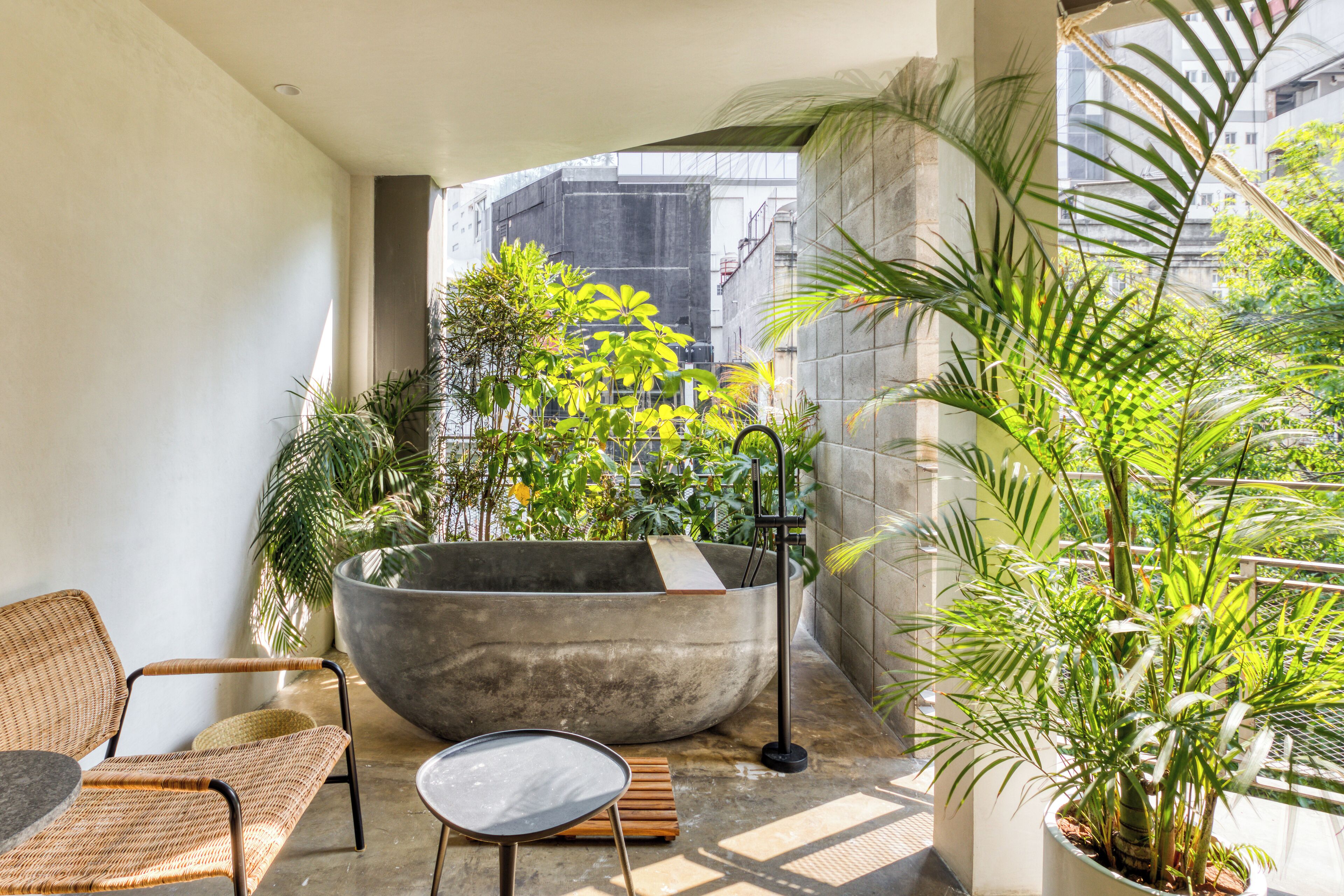 Ein Balkon mit einer großen Steinebadewanne, Korbmöbeln und Topfpflanzen.