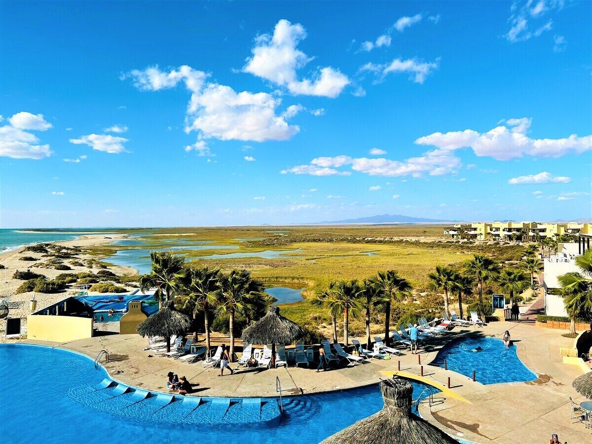 Un resort con varias piscinas, palmeras y vistas a la playa y al océano.