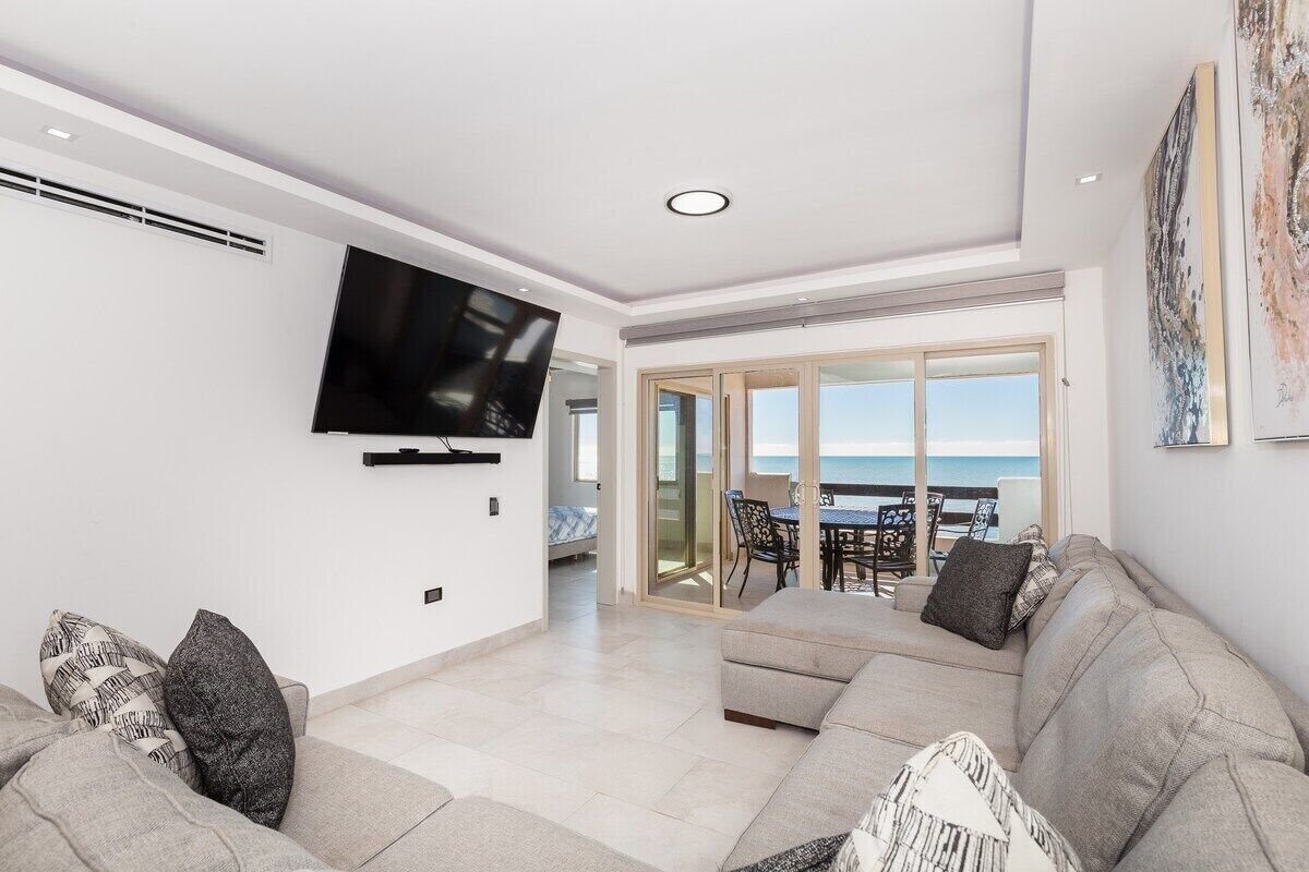 Una sala de estar moderna con televisor de pantalla plana, un sofá y un comedor con vistas al mar.