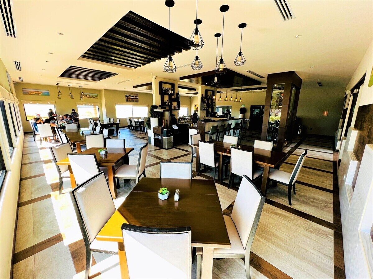 Um restaurante espaçoso com várias mesas e cadeiras, um espaço de bar e uma cozinha ao fundo.