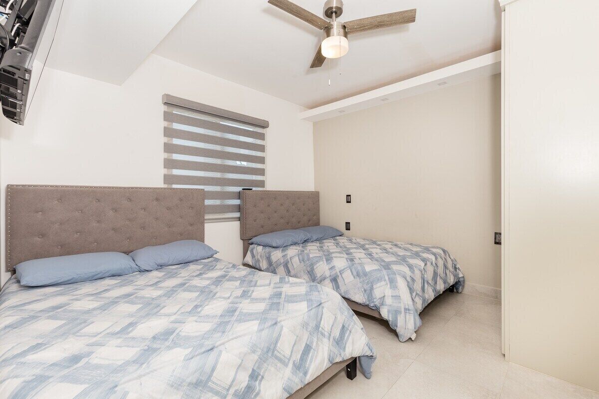 A bedroom with two beds, a ceiling fan, and a window with blinds.