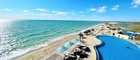 A beach with a swimming pool, sun loungers, and umbrellas.