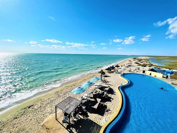 A beach with a swimming pool, sun loungers, and umbrellas.