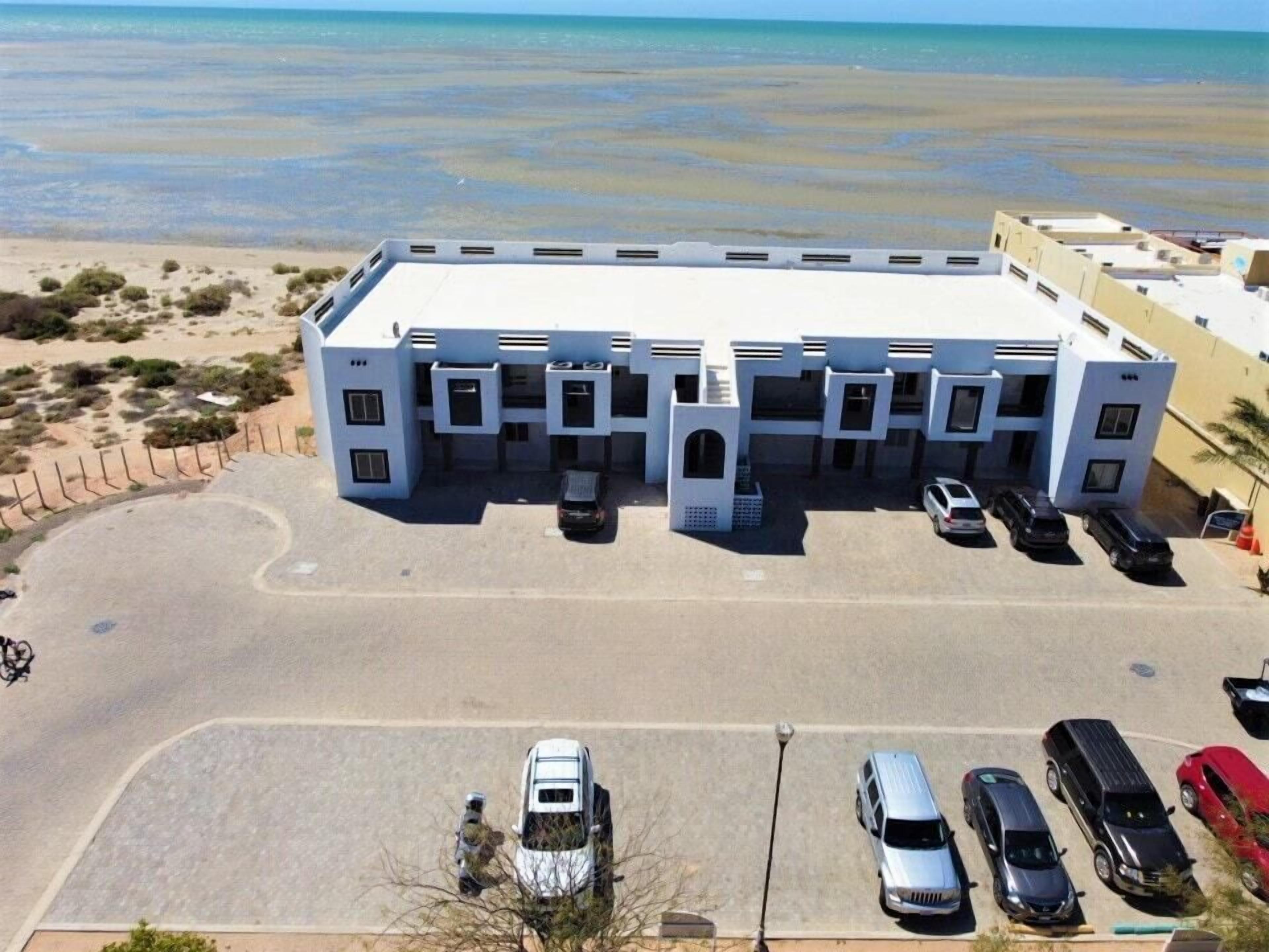 A modern building with a flat roof, multiple parking spaces, and a view of the beach.