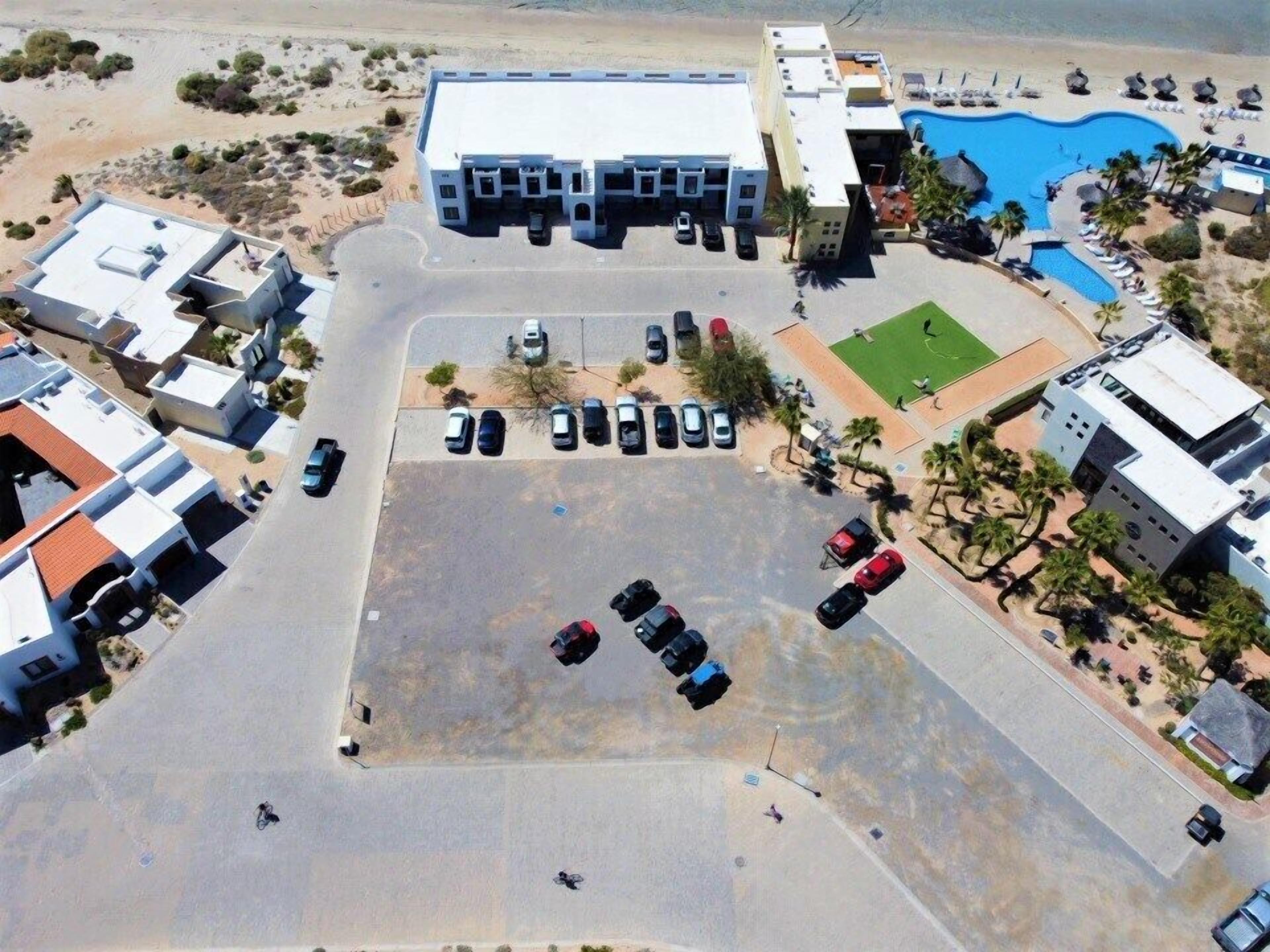 An aerial view of a resort with a swimming pool, multiple buildings, and a parking lot.