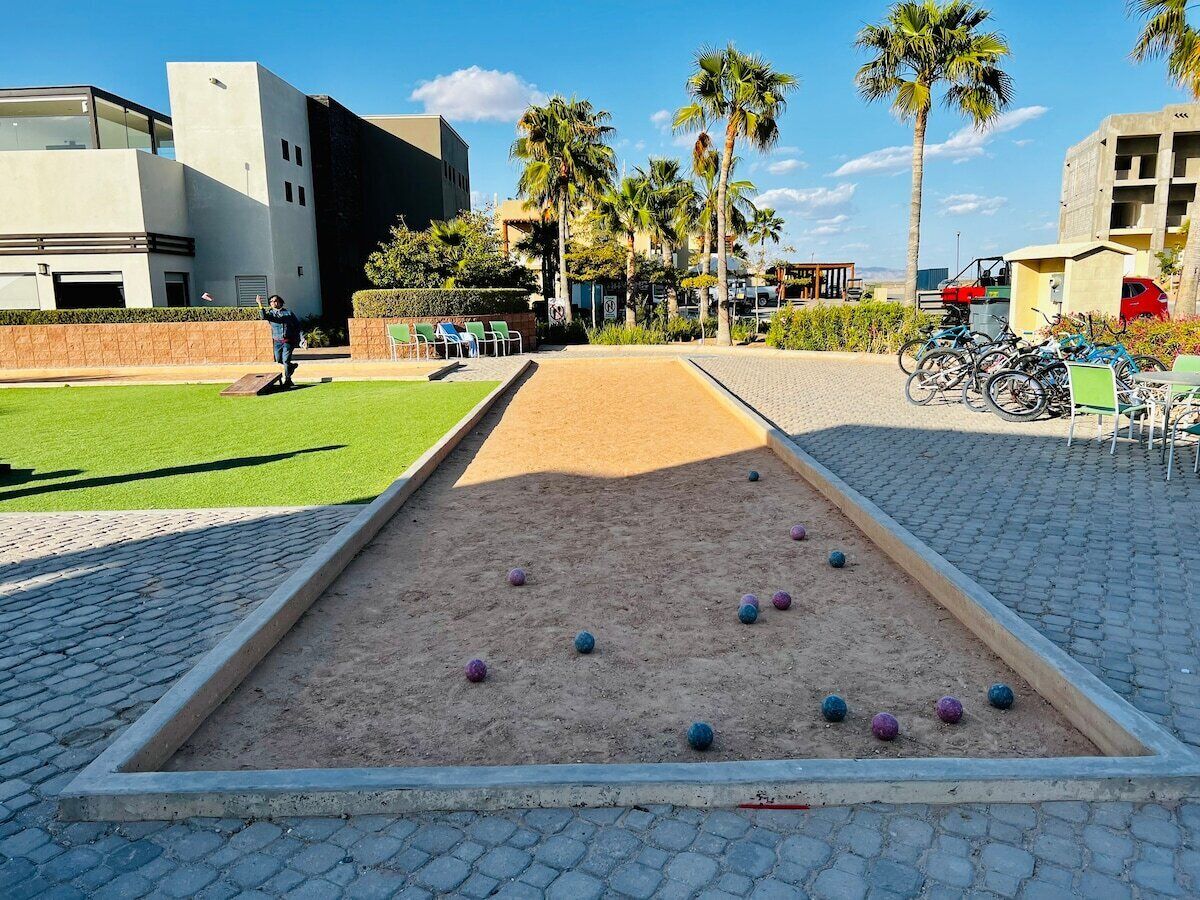 Een croquetbaan met zand, ballen en een verhard gebied met stoelen en fietsen.