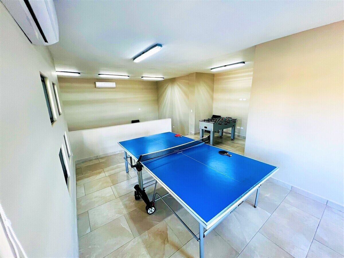 Una stanza con due tavoli da ping pong, un tavolo da calcio e una parete bianca con una finestra.