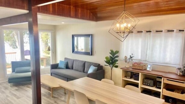 A modern living room with a wooden dining table, two chairs, a sofa, and a hanging light fixture. - Lakeside Cottage Getaway South Shore Lake Scugog

 (Caesarea)