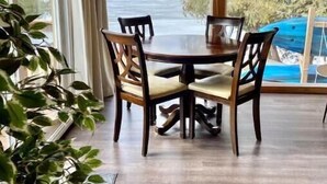 A dining area with a wooden table and chairs, large windows with curtains, and a view of a body of water. - Cozy Lakeside Cottage on Lake Scugog

 (Little Britain)