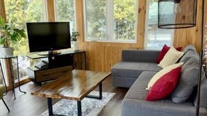 A cozy living room with a wooden interior, a flat-screen TV, a sofa with cushions, and a coffee table. - Cozy Lakeside Cottage on Lake Scugog

 (Little Britain)