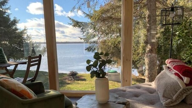 A cozy living room with a view of a lake, a wooden table with a vase, and a comfortable sofa. - Cozy Lakeside Cottage on Lake Scugog

 (Little Britain)