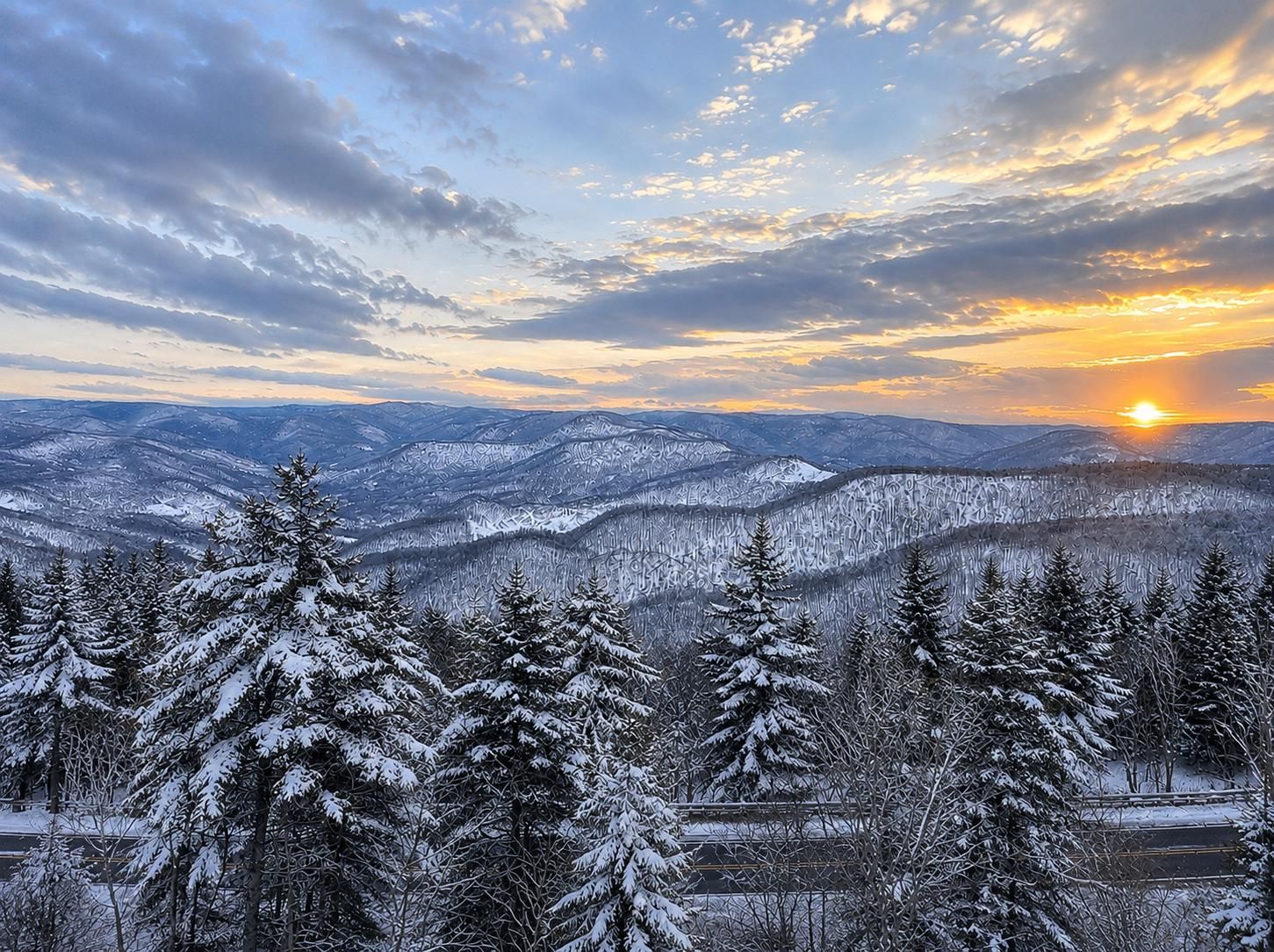 A mountainous landscape with snow-covered trees and a sunset in the background.