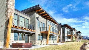A modern multi-story residential building with large windows, wooden balconies, and a stone facade.