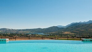 A swimming pool with clear blue water, surrounded by a wooden fence, and a mountainous landscape in the background.