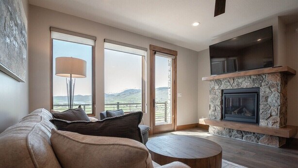 A living room with a stone fireplace, a large flat-screen TV, and a view of the outdoors.