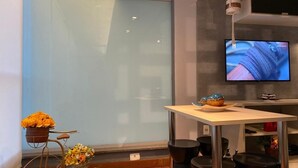 A modern room with a large window, a television mounted on the wall, a small table with a basket of flowers, and a bicycle with flowers.