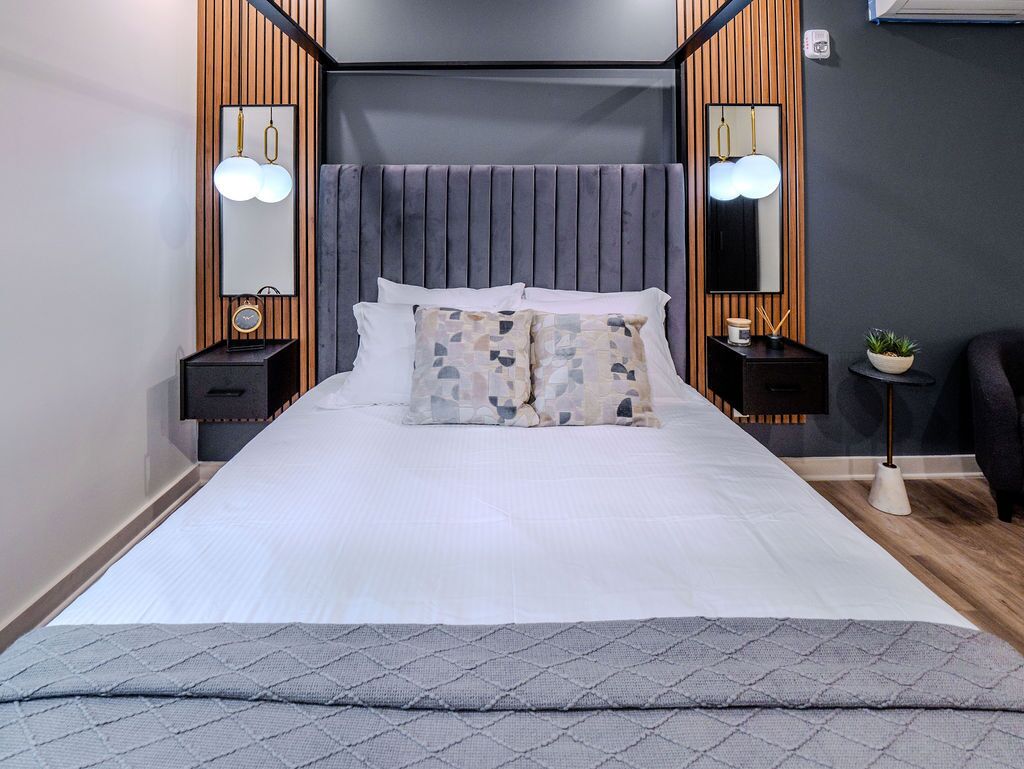 Een moderne slaapkamer met een groot bed, houten lambrisering, twee nachtkastjes met lampen en een kleine plant op het nachtkastje.
