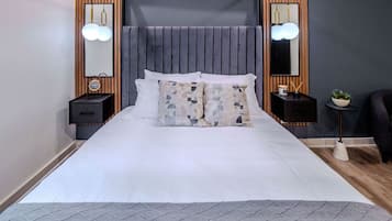 A modern bedroom with a large bed, wooden paneling, two bedside tables with lamps, and a small plant on the nightstand.