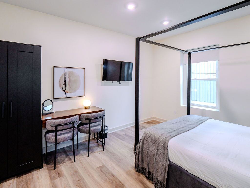 A bedroom with a bed, a desk with two chairs, a television, and a wardrobe.