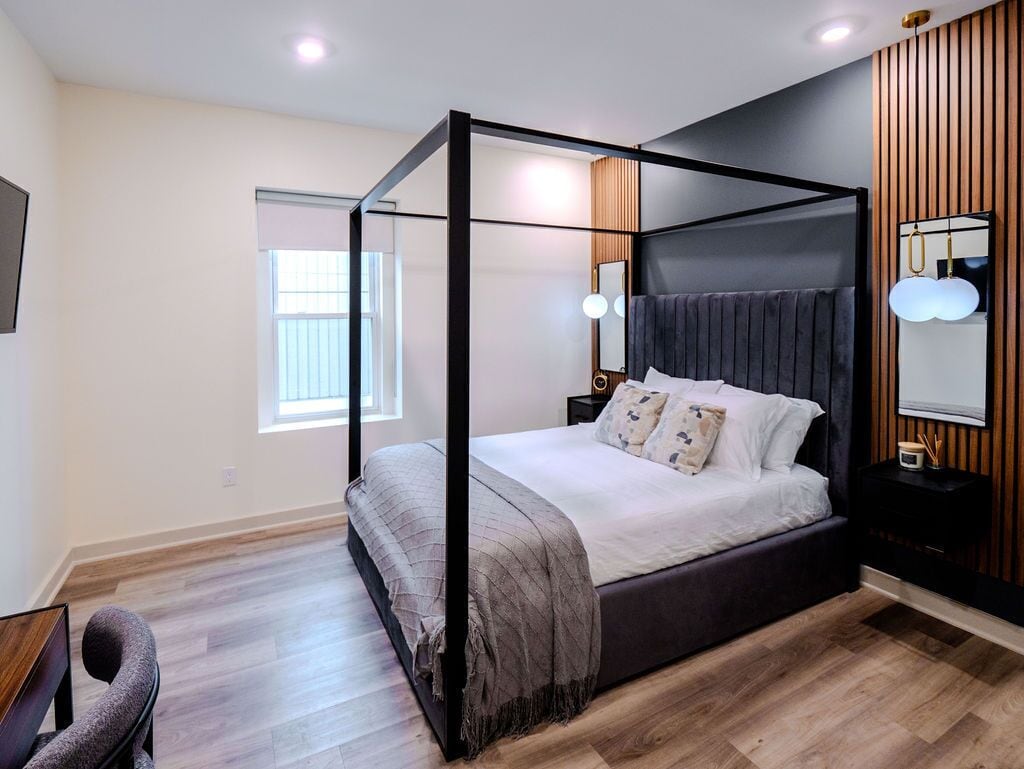 Un dormitorio moderno con cama con dosel, una mesita de noche, un espejo y una ventana.