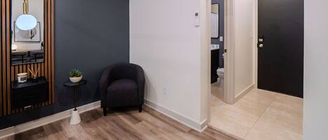 A modern living room with a dark wall, wooden floor, and a black door leading to a bathroom.