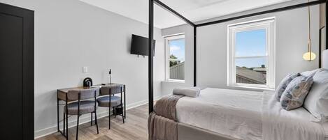 Un dormitorio con una cama con dosel, un escritorio con dos sillas, un televisor de pantalla plana y ventanas amplias.