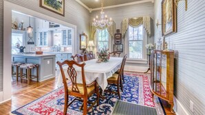 A dining area with a table set for four, surrounded by wooden chairs, a chandelier, and a patterned rug.