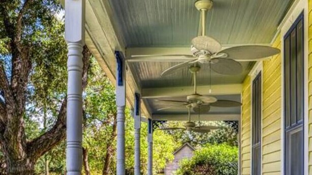 A covered porch with a railing, two rocking chairs, and a ceiling fan.