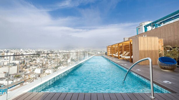 A rooftop infinity pool with a city view, wooden deck, and lounge area with chairs. - Ocean VIEW, Pool&Coworking, Queen Bed 19th floor (Barranco)