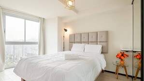 A modern bedroom with a large bed, a nightstand, a lamp, and a view of the city through a large window. - Ocean VIEW, Pool&Coworking, Queen Bed 19th floor (Barranco)