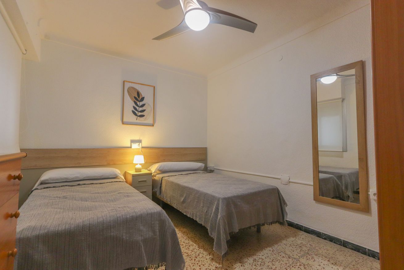 Un dormitorio con dos camas individuales, un ventilador de techo, una lámpara de noche, un cuadro en la pared y un espejo.